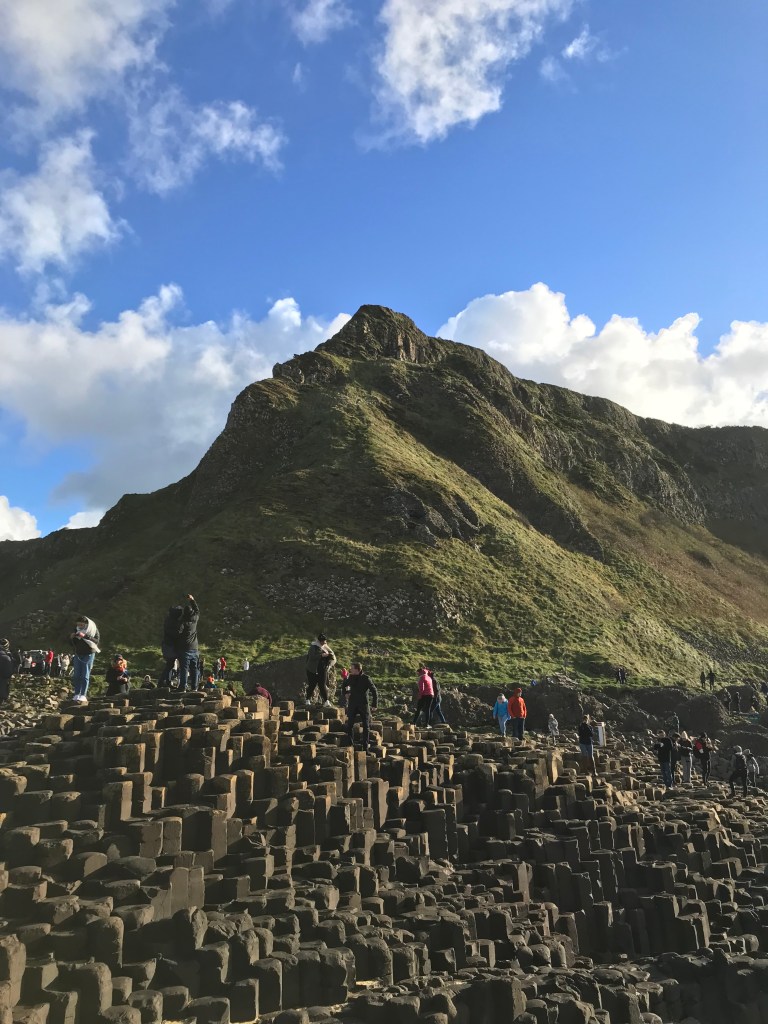 A landscape image of Giant's Causeway in Northern Ireland with tourists standing on the iconic rock formations.